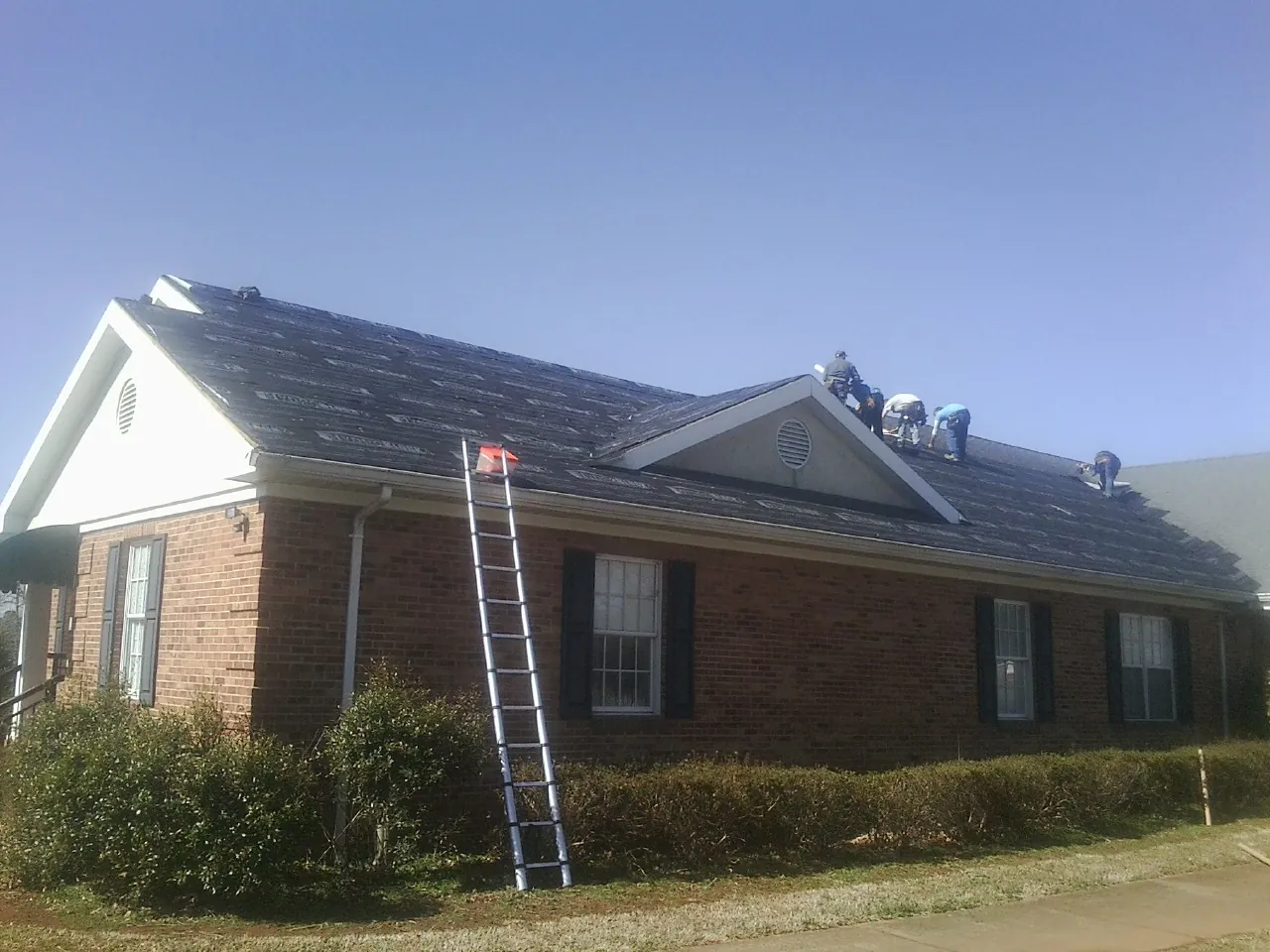 Crew tearing shingles off a brick ranch roof with a ladder set — Metal Roof Repair work by our crew in Centre Hall