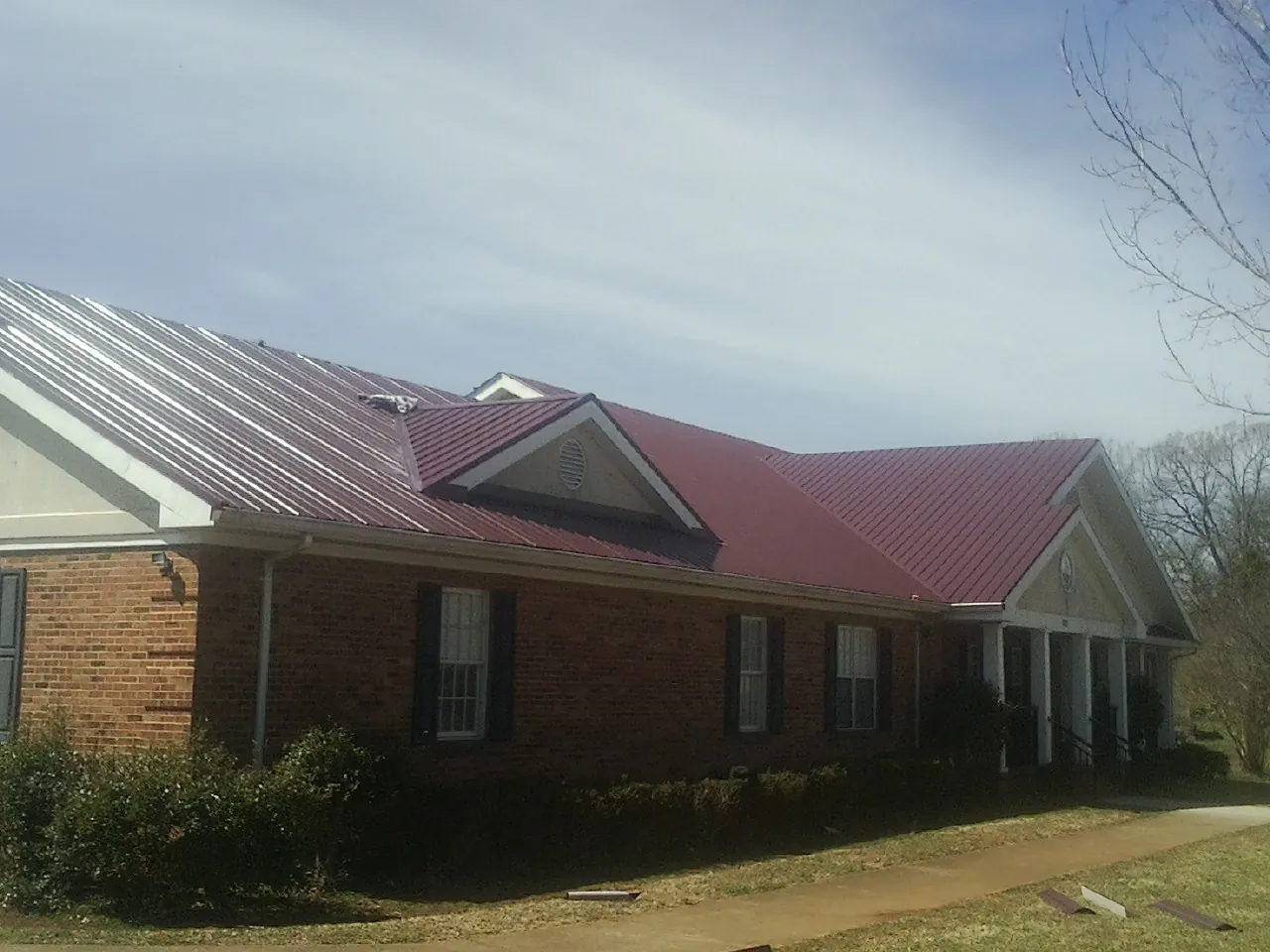 Red metal roof with gabled entries on a long brick building, from a Hail Damage Roof Repair job in Centre Hall