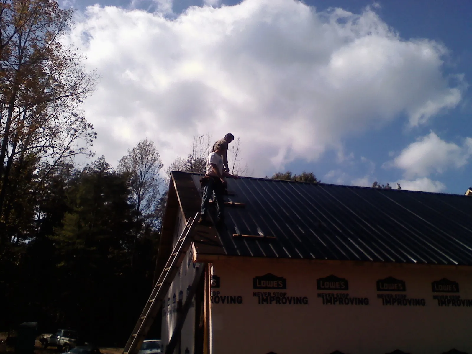 Roofer fastening dark metal panels high against a cloudy sky, from a Roof Inspection job in Centre Hall