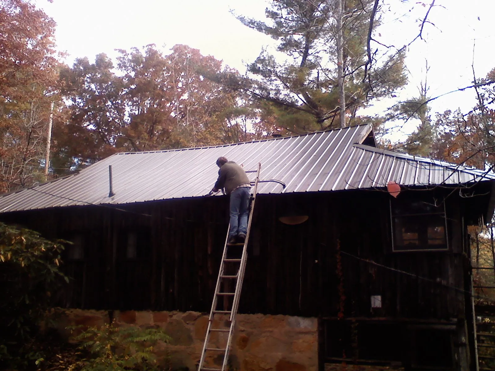 Roofer on a ladder working along the edge of a cabin metal roof in Centre Hall