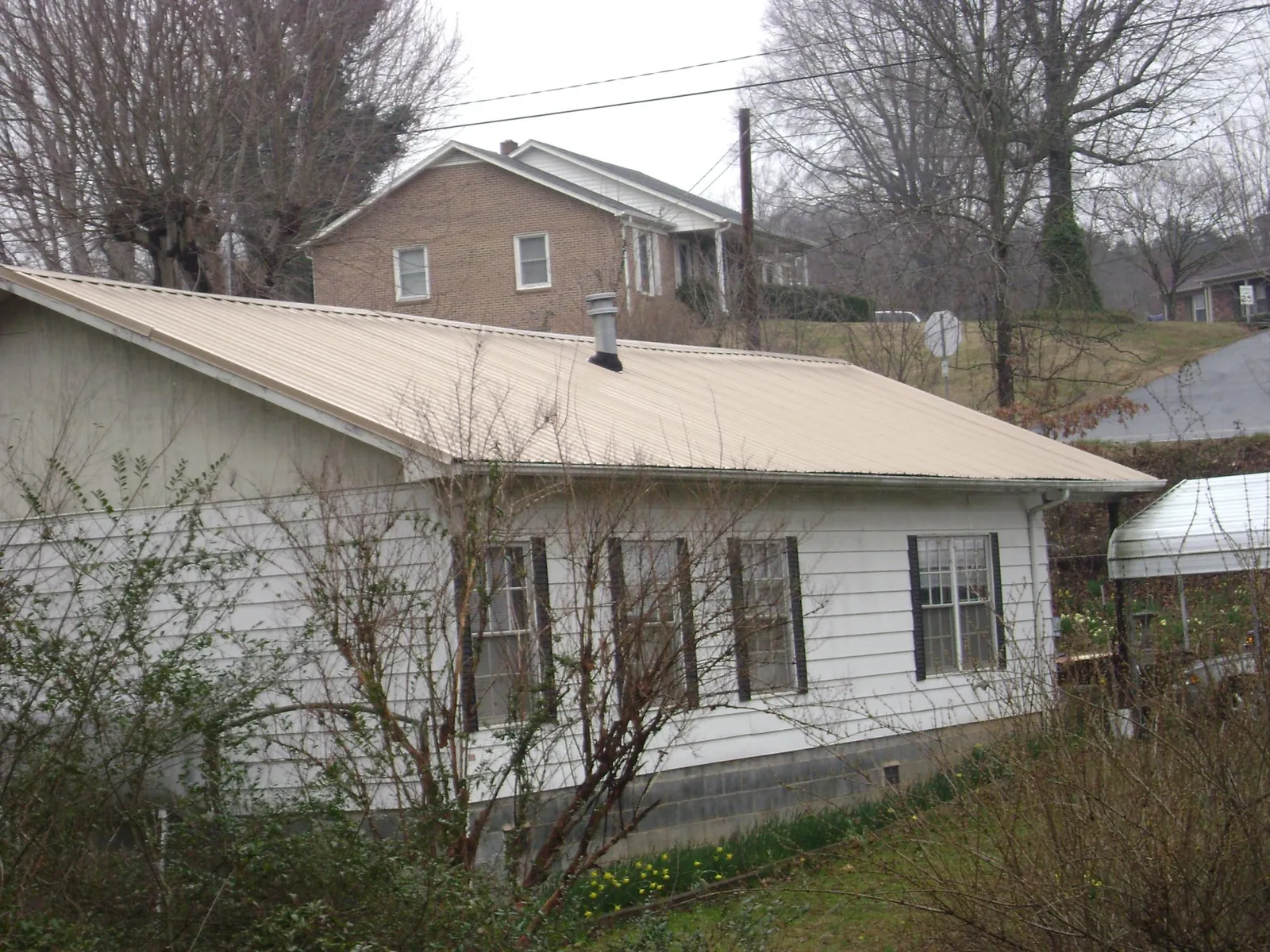Tan metal roof on a white sided house set into a hillside — Commercial Roofing by Roofing Brothers in Centre Hall